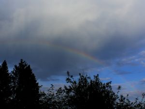 schwacher Regenbogen vor teilweise blauem Himmel
